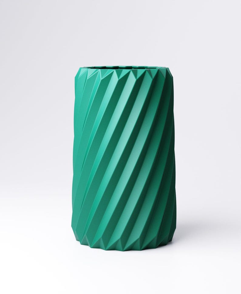 May include: A teal-colored, cylindrical vase with a geometric, ridged design. The vase has a textured surface with diagonal lines that create a spiral effect. The vase is a solid color and has a modern aesthetic.