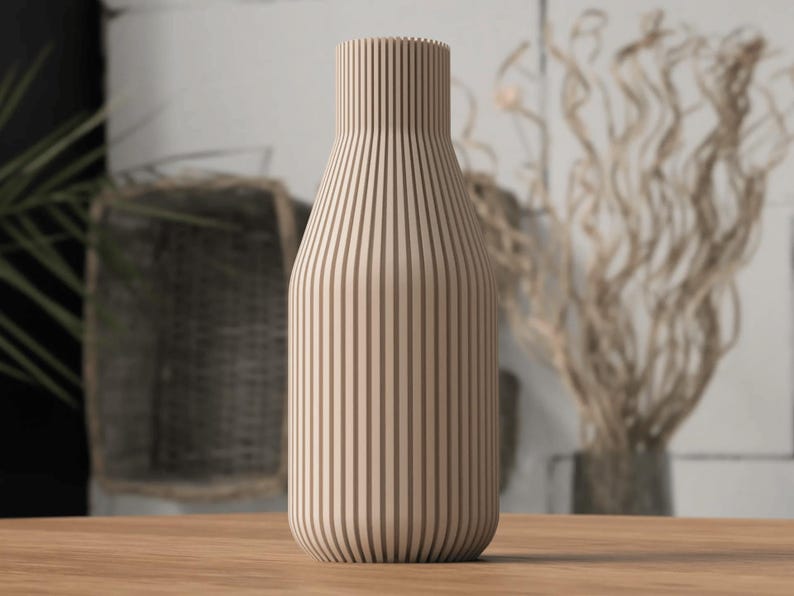 May include: A beige wooden vase with vertical brown stripes. The vase has a rounded base and a narrow neck. The vase is sitting on a wooden surface. The background includes a plant and decorative branches.