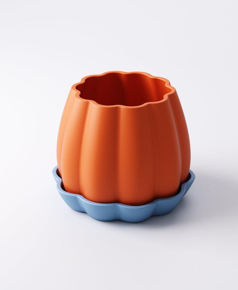 May include: An orange pumpkin-shaped planter with a wavy rim, sitting on a blue, scalloped saucer. The planter has vertical ridges and a smooth, matte finish. The design is simple and modern, suitable for indoor or outdoor use.