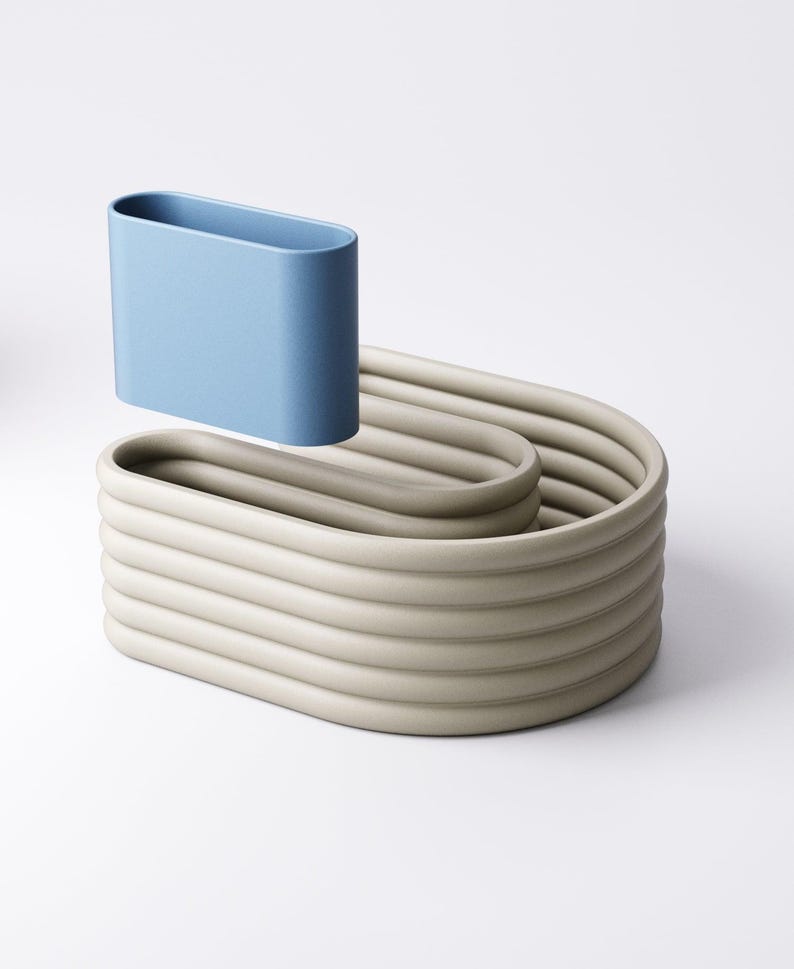 May include: A light blue, oval container hovers above a beige, wave-like, ribbed structure. The design has a minimalist aesthetic, with smooth, rounded forms and a neutral colour palette. The objects appear to be made of ceramic or a similar material.