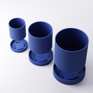 May include: Three blue cylindrical planters with a ribbed texture and matching circular bases are displayed against a white background. The planters are of varying sizes, with one detached from its base, showcasing a modern, minimalist design.