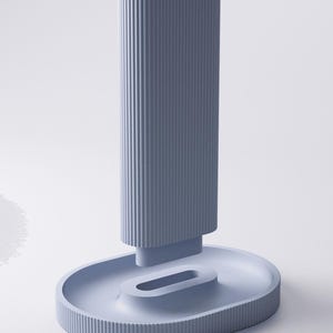 May include: A light blue vertical stand featuring a tall, rectangular column with a ribbed texture and a concave top. The column is attached to an oval-shaped base that includes a central, elongated, recessed slot and a matching ribbed outer edge.