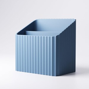 May include: A light blue desk organizer with a ribbed exterior design. The organizer has a slanted top and a divider inside, creating two compartments. The product is made of a solid material and is suitable for office or home use.