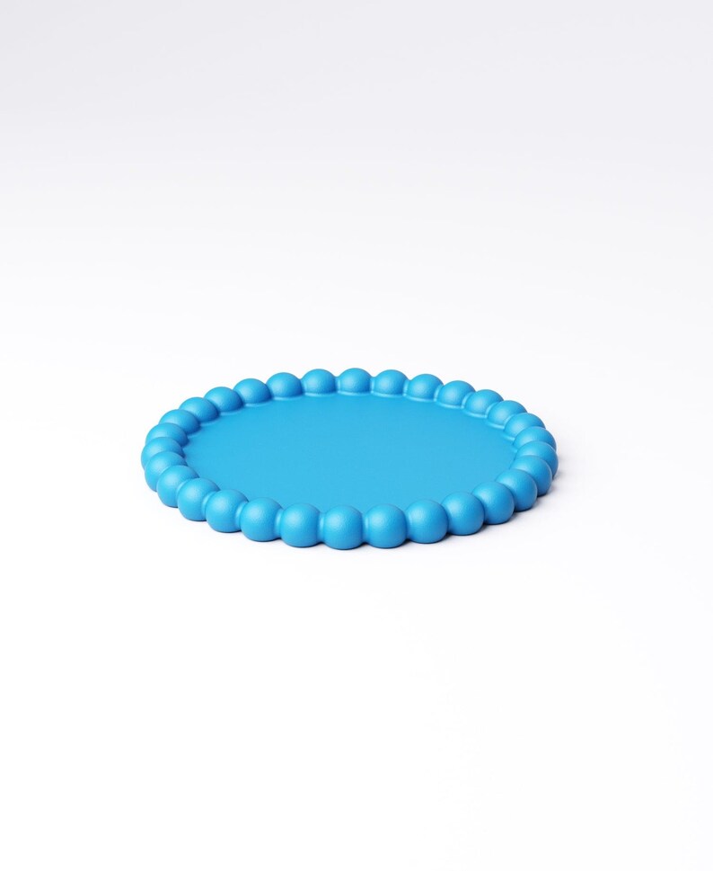 May include: A round, light blue tray with a beaded edge. The tray has a smooth, flat surface and a border of evenly spaced, rounded beads. The tray is set against a plain white background.
