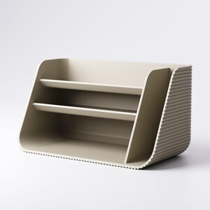 May include: A beige desk organizer with two shelves and a ribbed side panel. The organizer has a curved design and a minimalist aesthetic, suitable for office or home use.