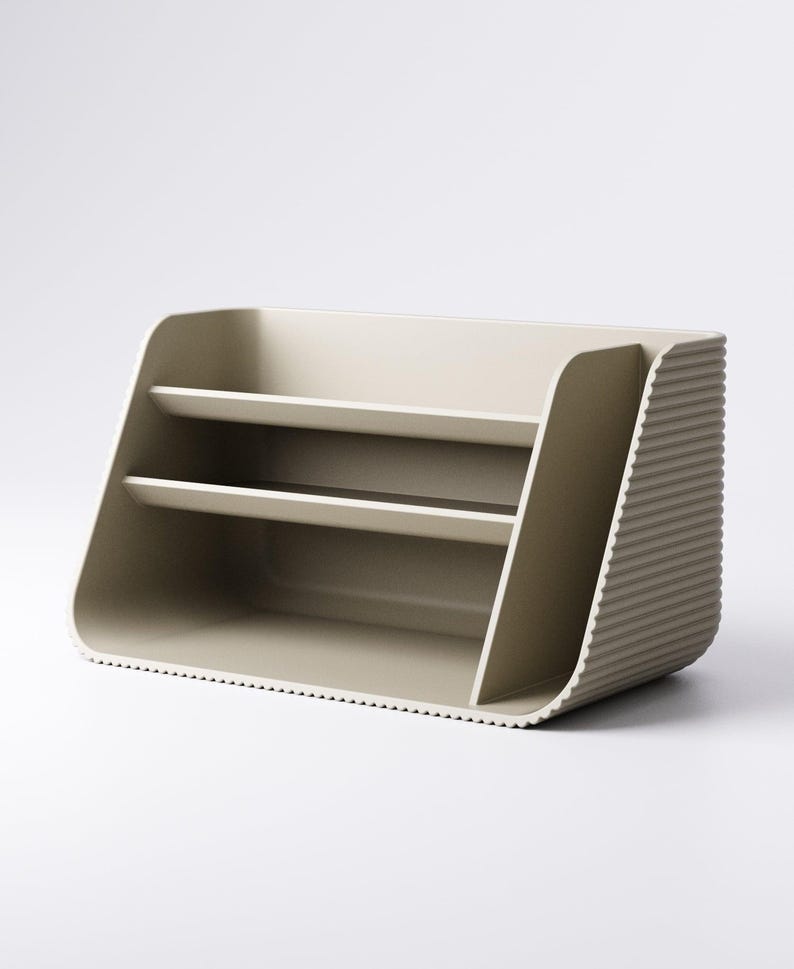 May include: A beige desk organizer with two shelves and a ribbed side panel. The organizer has a curved design and a minimalist aesthetic, suitable for office or home use.