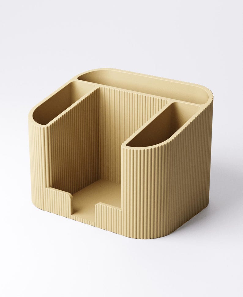 May include: A beige desk organizer with a ribbed texture. The organizer has three compartments: two angled slots and a central open area. The design is modern and minimalist, suitable for office or home use.