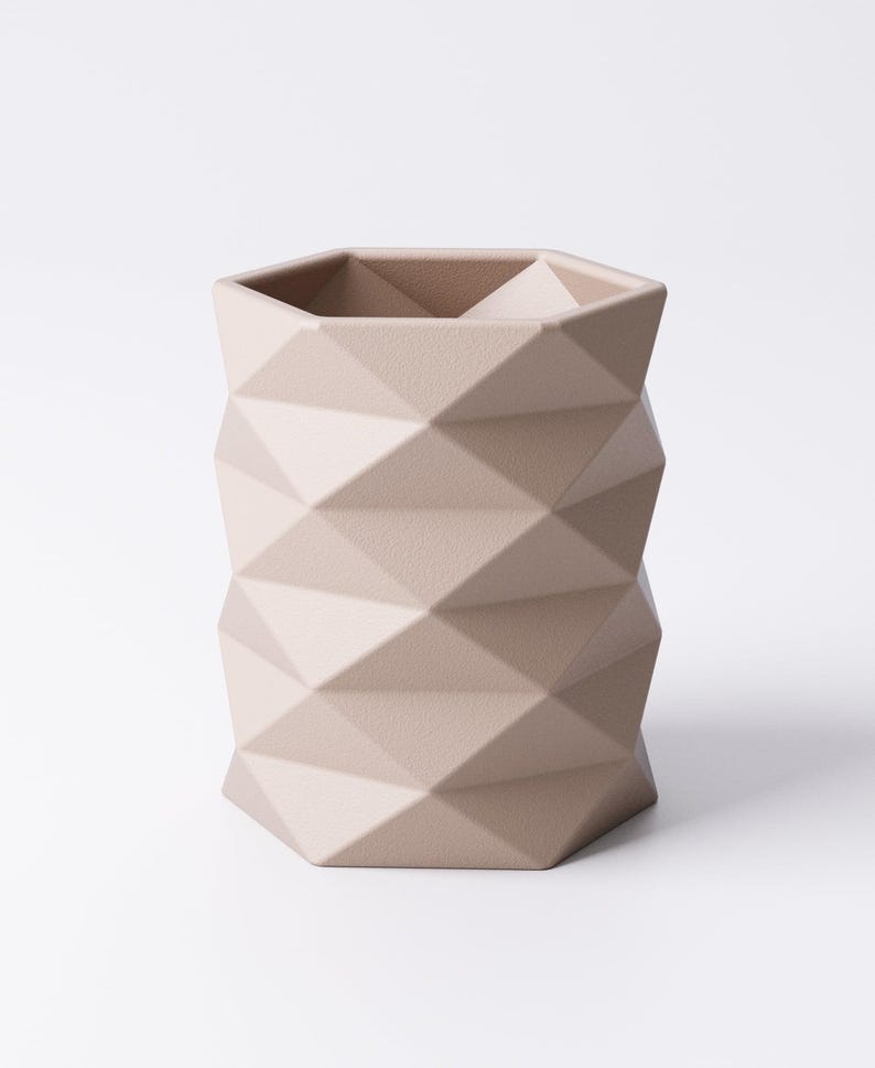 May include: A beige geometric vase with a faceted design. The vase has a hexagonal top and a textured surface. The neutral color and modern design make it a versatile decorative piece.