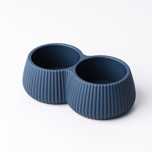 May include: A navy blue, double-bowl container with a ribbed exterior. The two circular bowls are connected, creating a unique shape. The container is made of a solid material and is suitable for various uses.