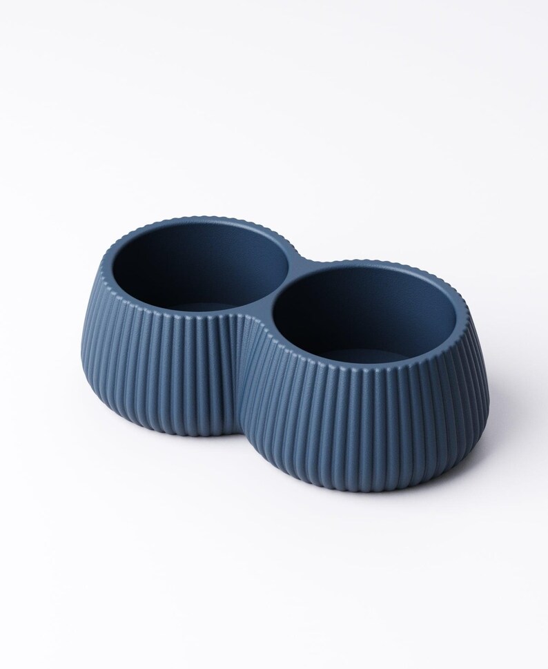 May include: A navy blue, double-bowl container with a ribbed exterior. The two circular bowls are connected, creating a unique shape. The container is made of a solid material and is suitable for various uses.