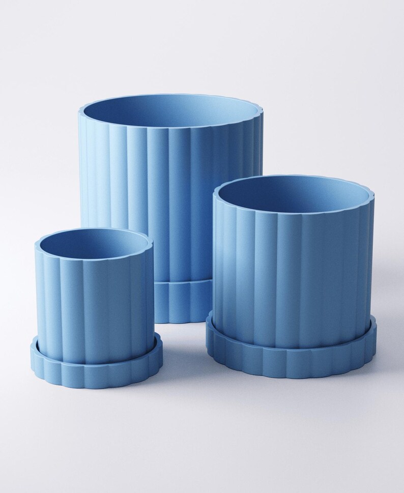 May include: Three light blue cylindrical planters of varying sizes. Each planter has vertical ridged detailing and sits on a matching round base. The planters are empty and ready for plants. The background is plain white.