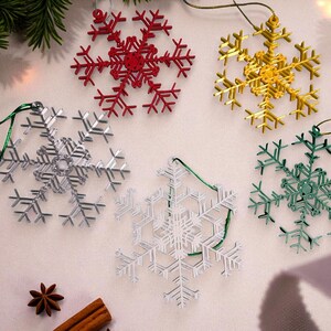May include: A collection of snowflake ornaments in red, gold, silver, white, and green. Each ornament is a detailed, openwork design with a string for hanging. Festive holiday decor.