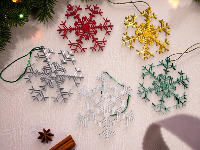 May include: A collection of snowflake ornaments in red, gold, silver, white, and green. Each ornament is a detailed, openwork design with a string for hanging. Festive holiday decor.