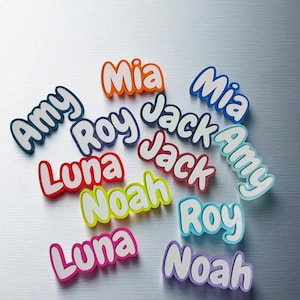 May include: A collection of colorful name cutouts, including "Amy," "Mia," "Jack," "Roy," "Luna," and "Noah." Each name is in a different color, with a white outline, and set against a metallic silver background.