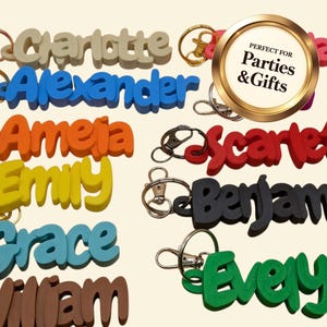 May include: A collection of colorful name keychains in various colors, including beige, blue, orange, yellow, red, black, teal, and brown. Each keychain features a different name in a bold, 3D font, attached to a metal keyring.