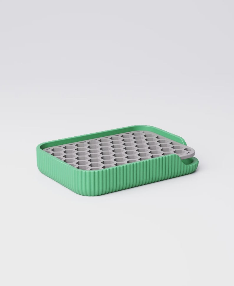 May include: A rectangular ice cube tray with a green ribbed border and a gray interior with multiple hexagonal molds. The tray has a small handle on one side. The design is modern and minimalist.