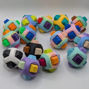 May include: A collection of colorful, geometric puzzle balls. Each ball features a cube shape with various colored squares and cube-shaped pieces. The color palette includes blue, orange, purple, green, and yellow.