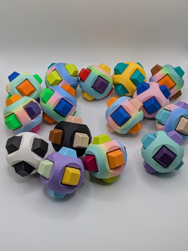 May include: A collection of colorful, geometric puzzle balls. Each ball features a cube shape with various colored squares and cube-shaped pieces. The color palette includes blue, orange, purple, green, and yellow.