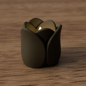 May include: A dark brown, tulip-shaped candle holder with a lit candle inside. The holder has a textured surface and sits on a wooden surface. The candle holder's petals are slightly open, revealing the warm glow of the candle.
