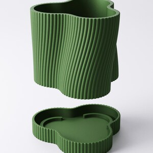 May include: A green, clover-shaped container and lid set. The container has a textured, vertical, ridged design that twists. The lid is a matching green with a clover shape and a recessed interior.