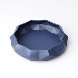 Puede incluir: Un cuenco azul marino con un dise&ntilde;o geom&eacute;trico facetado. El cuenco tiene una forma ancha y poco profunda con una base plana y lados angulados. El cuenco est&aacute; hecho de un material s&oacute;lido y est&aacute; sobre un fondo blanco.