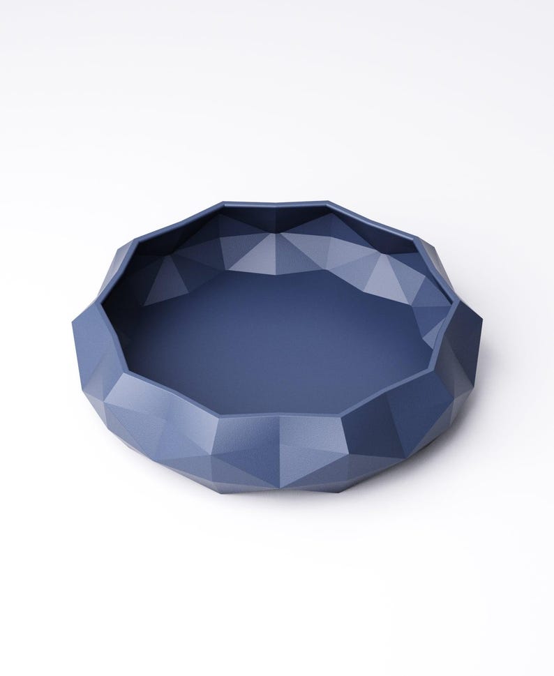 Puede incluir: Un cuenco azul marino con un dise&ntilde;o geom&eacute;trico facetado. El cuenco tiene una forma ancha y poco profunda con una base plana y lados angulados. El cuenco est&aacute; hecho de un material s&oacute;lido y est&aacute; sobre un fondo blanco.