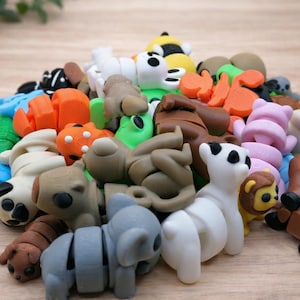 May include: A collection of colorful animal-shaped erasers in various colors, including white, brown, orange, green, and blue. The erasers are arranged on a light brown wooden surface. The assortment includes a panda, koala, lion, and bear.