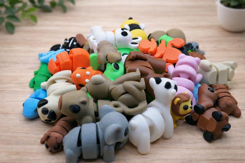 May include: A collection of colorful animal-shaped erasers in various colors, including white, brown, orange, green, and blue. The erasers are arranged on a light brown wooden surface. The assortment includes a panda, koala, lion, and bear.