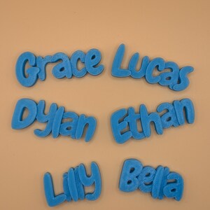 May include: Six blue 3D-printed name cutouts: Grace, Lucas, Dylan, Ethan, Lily, and Bella. The names are in a playful, rounded font, and are displayed against a light tan background. Ideal for personalized gifts or room decor.