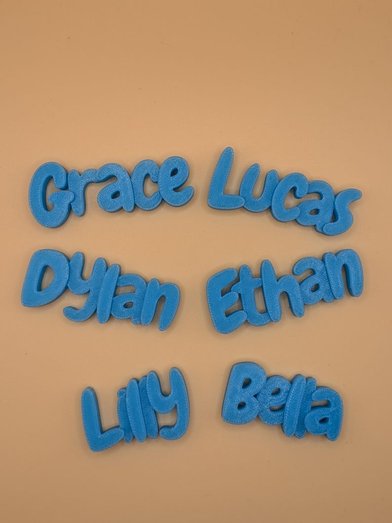 May include: Six blue 3D-printed name cutouts: Grace, Lucas, Dylan, Ethan, Lily, and Bella. The names are in a playful, rounded font, and are displayed against a light tan background. Ideal for personalized gifts or room decor.