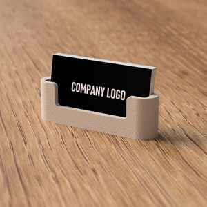 May include: A business card holder with a black card that reads "COMPANY LOGO" in white. The holder is a light beige color and is sitting on a wooden surface.
