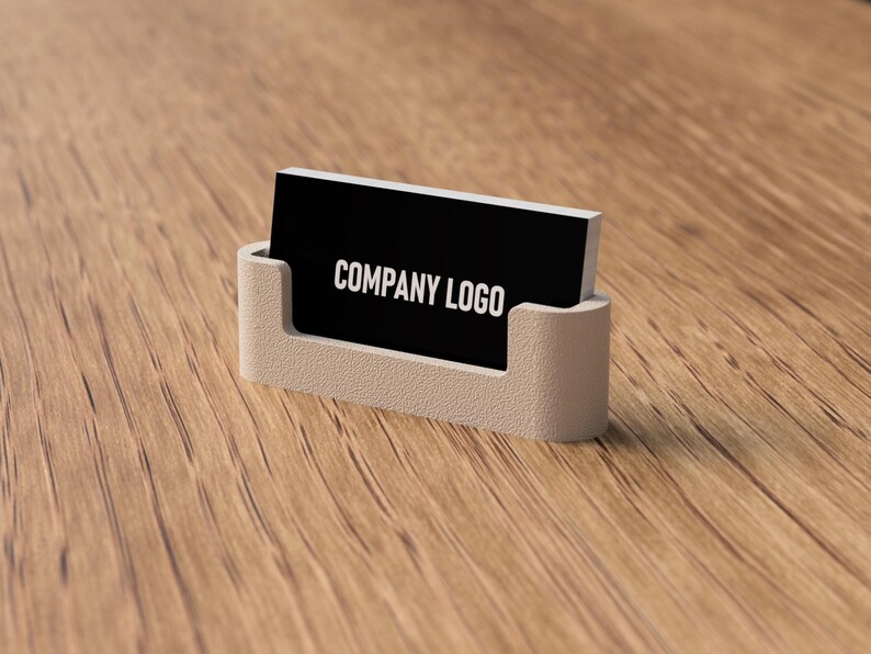 May include: A business card holder with a black card that reads "COMPANY LOGO" in white. The holder is a light beige color and is sitting on a wooden surface.