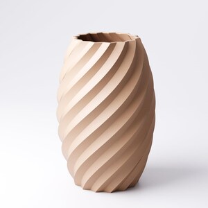 May include: A beige, decorative vase with a spiral design. The vase has a wide, oval shape and a textured surface created by the diagonal grooves. The top edge of the vase has a wavy, irregular pattern.