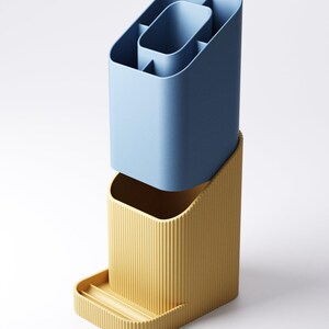 May include: A two-piece desk organizer in a modern design. The top section is a light blue, multi-compartment container. The bottom section is a yellow-tan color with vertical ridges and a small tray. The organizer is made of plastic.