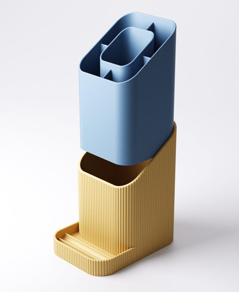 May include: A two-piece desk organizer in a modern design. The top section is a light blue, multi-compartment container. The bottom section is a yellow-tan color with vertical ridges and a small tray. The organizer is made of plastic.