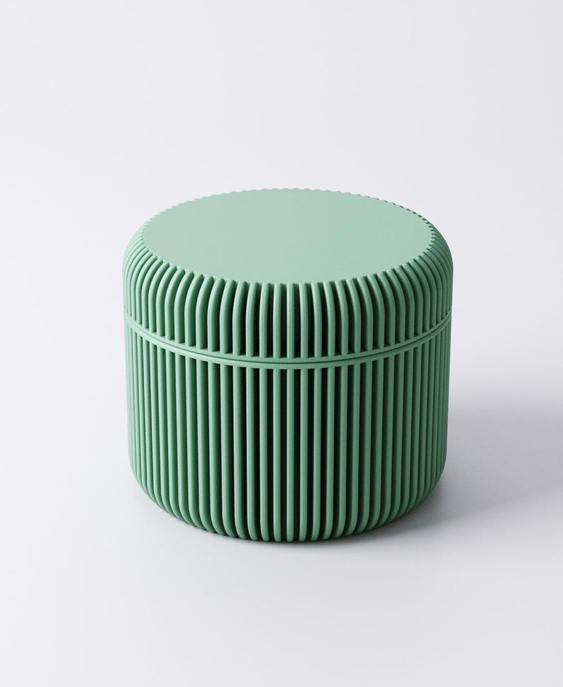 May include: A mint green, cylindrical container with a lid. The container's body features vertical, ridged detailing, and the lid has a flat, textured surface. The design is minimalist and modern, suitable for storage or decorative purposes.