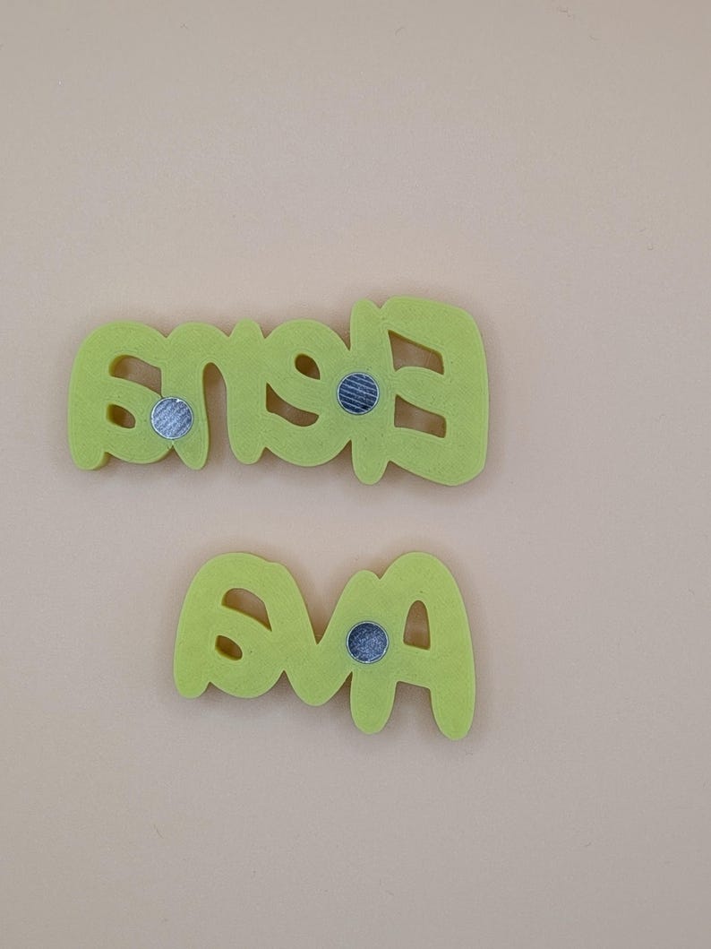 May include: Two lime green felt name magnets spelling "Eva" and "Eves" with silver magnets on the back. The letters are in a playful, rounded font. The background is a solid, light beige colour.