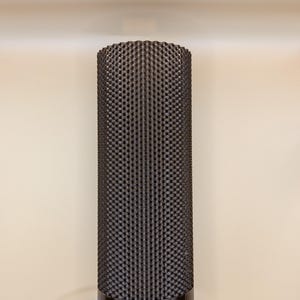 K&ouml;nnte beinhalten: Eine zylindrische Lampe mit einer strukturierten, dunkelbraunen Au&szlig;enseite. Die Lampe hat ein dunkelbraunes Band oben und einen hellblauen Sockel. Ein hellblaues Kabel erstreckt sich von der Basis. Die Lampe ist ein modernes Design.