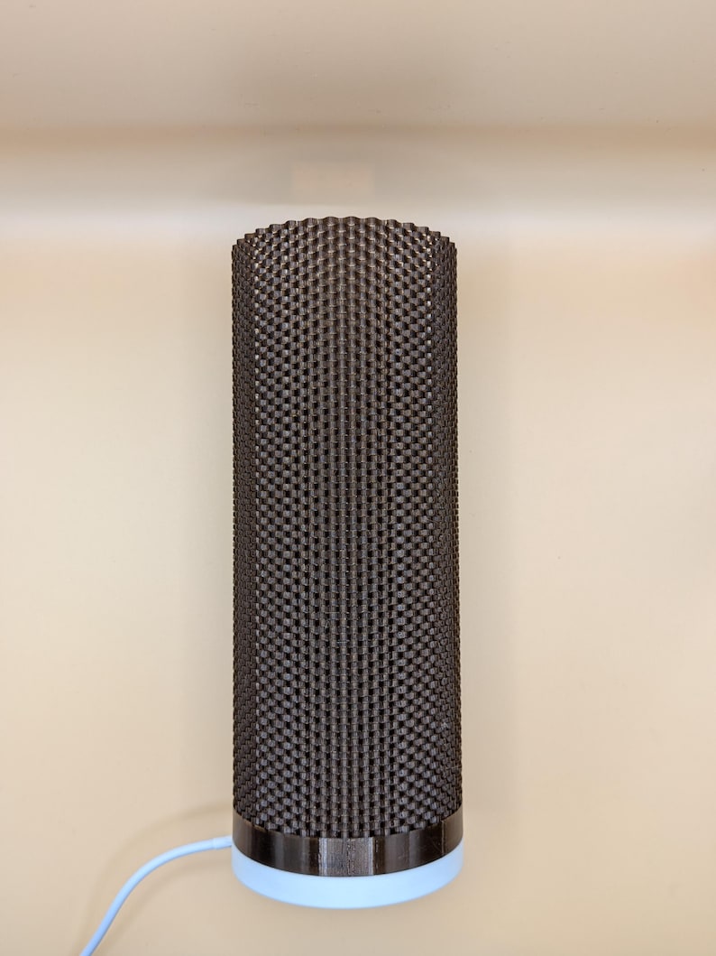 K&ouml;nnte beinhalten: Eine zylindrische Lampe mit einer strukturierten, dunkelbraunen Au&szlig;enseite. Die Lampe hat ein dunkelbraunes Band oben und einen hellblauen Sockel. Ein hellblaues Kabel erstreckt sich von der Basis. Die Lampe ist ein modernes Design.