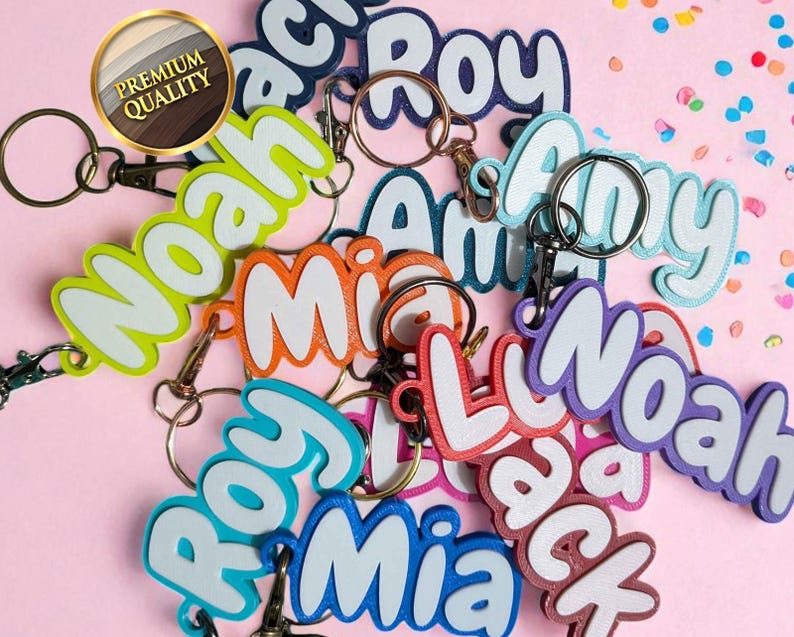 May include: A collection of colorful name keychains with white outlines and metal key rings. The names include "Noah", "Mia", "Roy", "Amy", and "Jack". The keychains are in various colors, including green, orange, blue, and purple.
