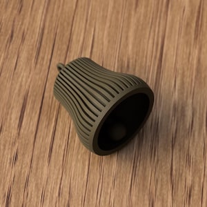 May include: A dark olive green bell-shaped object with vertical, curved lines. The object has a small loop at the top and a dark interior. It is resting on a wooden surface.