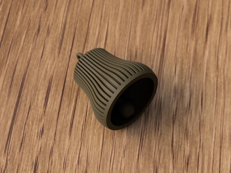 May include: A dark olive green bell-shaped object with vertical, curved lines. The object has a small loop at the top and a dark interior. It is resting on a wooden surface.