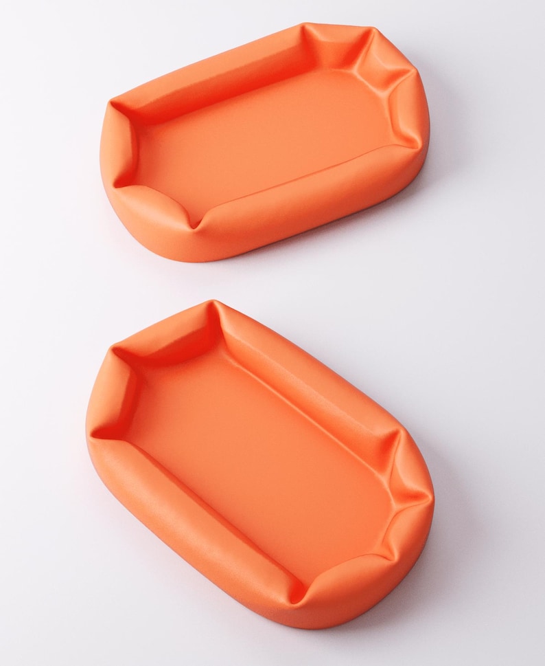 May include: Two orange, rectangular trays with rounded corners are displayed against a white background. The trays have a soft, puffy appearance, with the edges slightly gathered. The color is a vibrant, solid orange.
