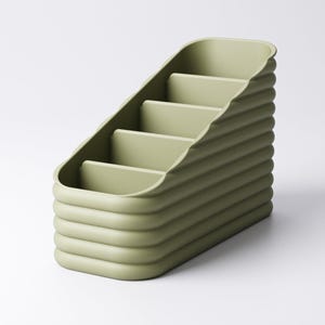 May include: A sage green desk organizer with a stepped design. The organizer has four compartments and a ribbed exterior. The overall shape is rectangular with rounded edges. The product is made of a solid, matte material.