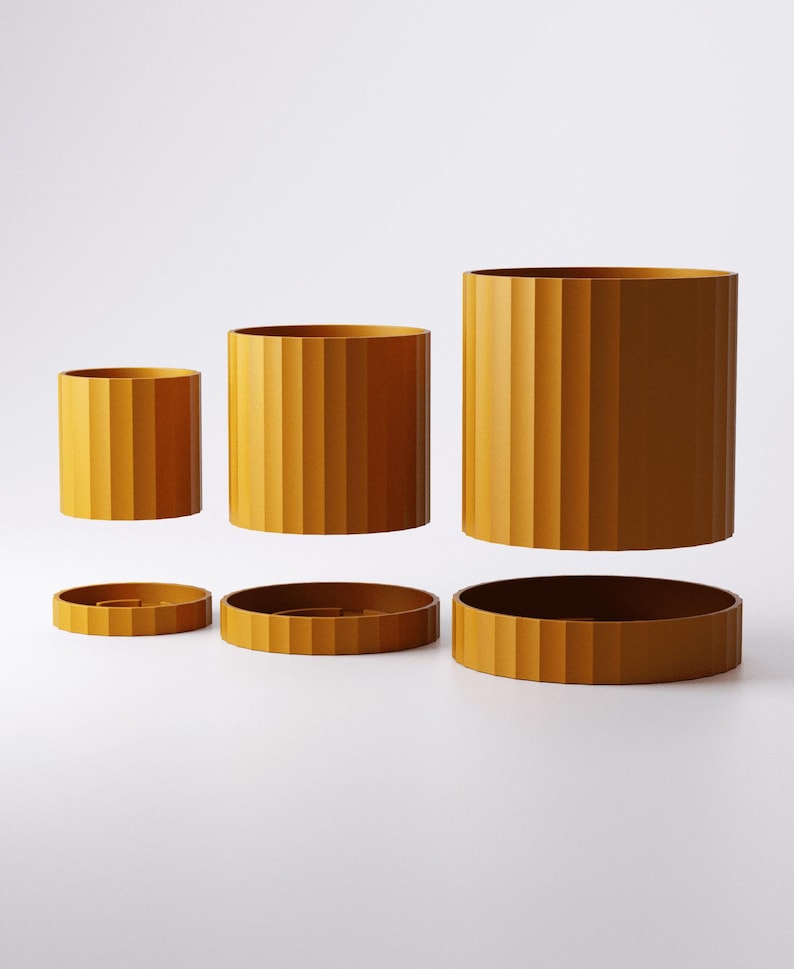 Puede incluir: Tres macetas cil&iacute;ndricas de color amarillo mostaza con texturas acanaladas verticales, cada una acompa&ntilde;ada de una base circular a juego. Las macetas est&aacute;n dispuestas en fila, aumentando de tama&ntilde;o de izquierda a derecha, con cada maceta suspendida sobre su base.