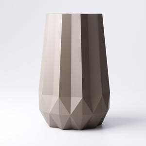 K&ouml;nnte beinhalten: Eine hohe, geometrische Vase in Graut&ouml;nen. Die Vase hat ein facettiertes Design am Boden und vertikale Rippen am K&ouml;rper. Die neutrale Farbpalette und die moderne Form machen sie zu einem vielseitigen Dekorationsst&uuml;ck.