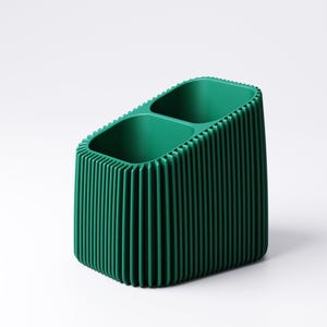 May include: A green desk organizer with two compartments. The organizer has a ribbed exterior and a rectangular shape. The interior is smooth, and the exterior has vertical lines. The organizer is made of a solid, opaque material.