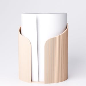 K&ouml;nnte beinhalten: Ein moderner, zylindrischer Papierhandtuchhalter. Der Halter ist hellbeige mit vertikalen Rippendetails an der Au&szlig;enseite. Das Design hat eine geschwungene Form, die sich teilweise um eine Rolle wei&szlig;er Papierhandt&uuml;cher legt.