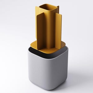 May include: A contemporary container set comprising two pieces. The base is a grey, vertically-lined, square-shaped container. The top piece is a mustard-yellow, open-topped, square-shaped container with four vertical fins.