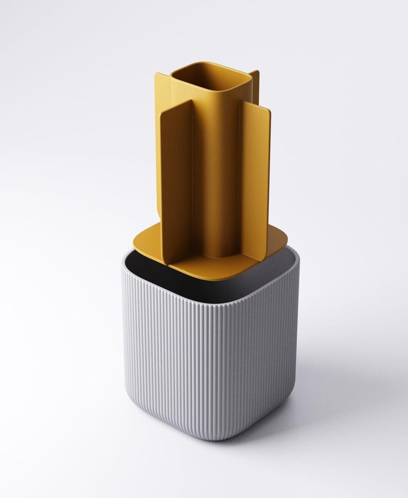 May include: A contemporary container set comprising two pieces. The base is a grey, vertically-lined, square-shaped container. The top piece is a mustard-yellow, open-topped, square-shaped container with four vertical fins.